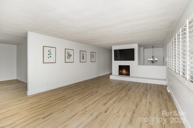 unfurnished living room featuring a chandelier, wood finished floors, a fireplace, and baseboards