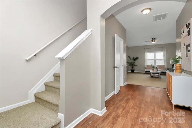 interior space featuring arched walkways, visible vents, wood finished floors, baseboards, and stairs