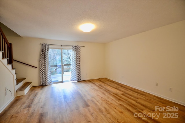 unfurnished room with light wood-style floors, a textured ceiling, baseboards, and stairs