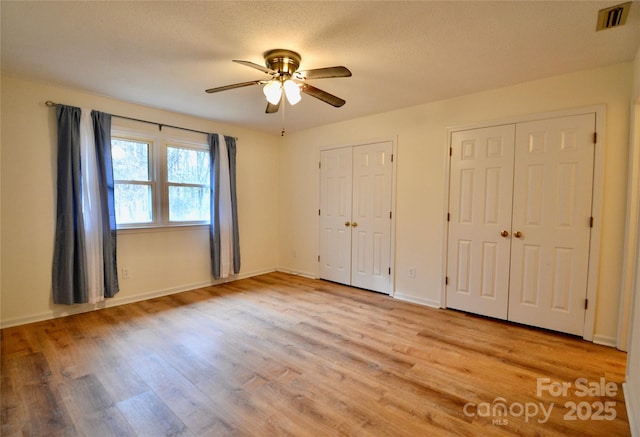 unfurnished bedroom with multiple closets, ceiling fan, light hardwood / wood-style floors, and a textured ceiling