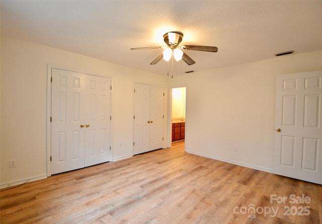 unfurnished bedroom featuring two closets, light hardwood / wood-style floors, and ceiling fan