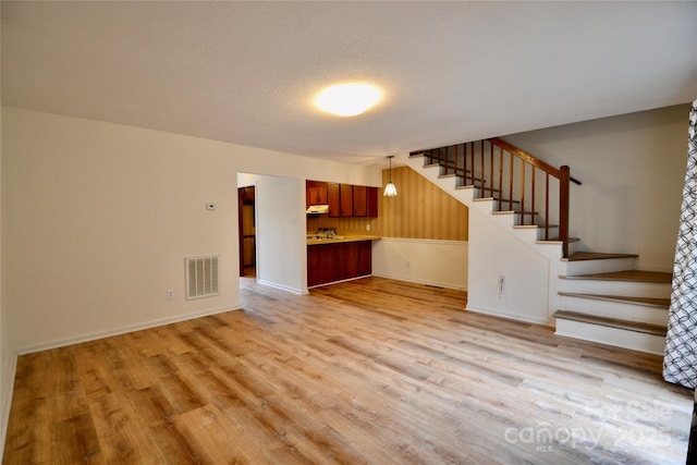 unfurnished living room with visible vents, light wood-style flooring, a textured ceiling, and stairs