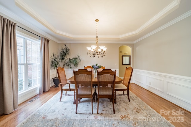 dining area featuring light wood-type flooring, visible vents, arched walkways, and wainscoting