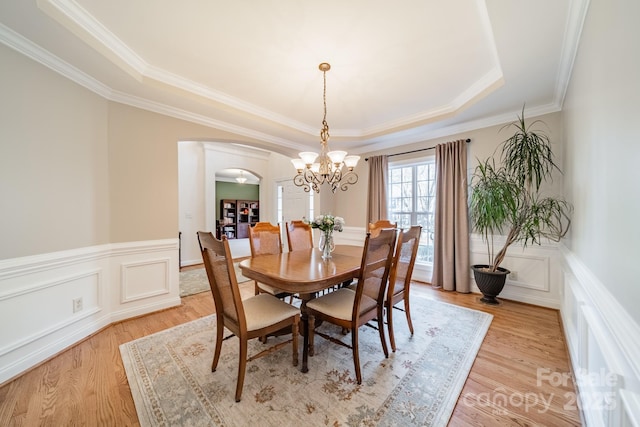 dining area featuring light wood-style flooring, arched walkways, a tray ceiling, and wainscoting