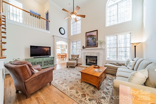 living room with ceiling fan, light wood-style flooring, a premium fireplace, stairway, and crown molding