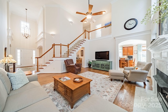 living room featuring arched walkways, a fireplace, light wood finished floors, ornamental molding, and stairs