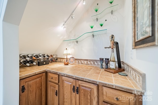 kitchen with rail lighting, brown cabinets, and vaulted ceiling