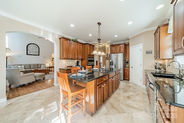 kitchen featuring arched walkways, stainless steel appliances, a sink, a center island, and brown cabinetry