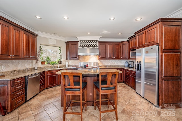 kitchen with a center island, light stone countertops, ornamental molding, appliances with stainless steel finishes, and a kitchen breakfast bar