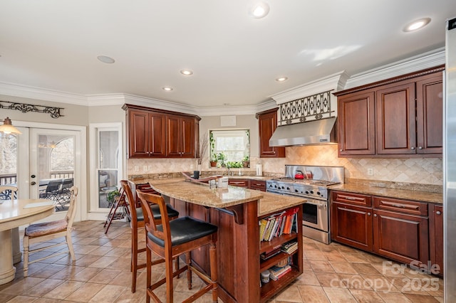 kitchen with light stone counters, a kitchen breakfast bar, crown molding, wall chimney exhaust hood, and range with two ovens