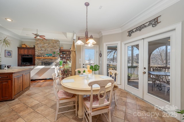 dining area featuring ceiling fan, ornamental molding, a stone fireplace, and french doors