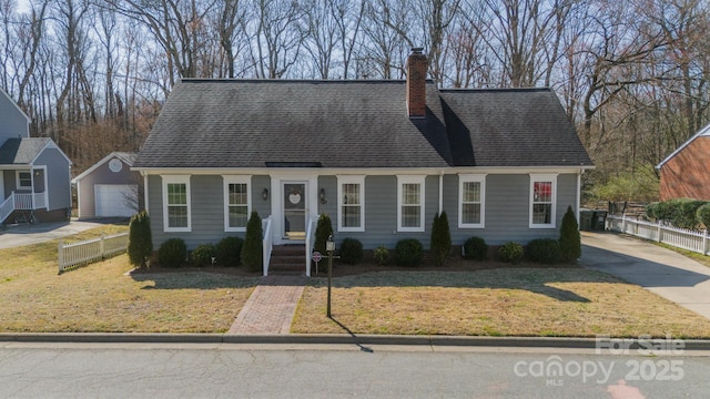 cape cod home featuring a front lawn, fence, a chimney, a garage, and an outbuilding