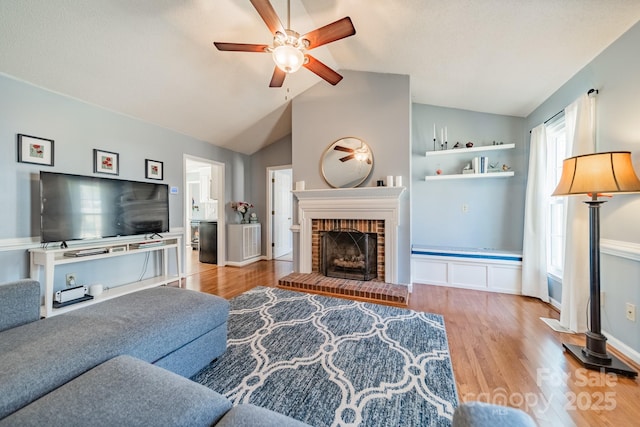 living area with a ceiling fan, lofted ceiling, a brick fireplace, and wood finished floors