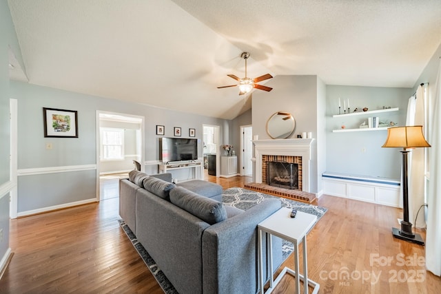 living room with a ceiling fan, light wood-type flooring, a brick fireplace, and lofted ceiling