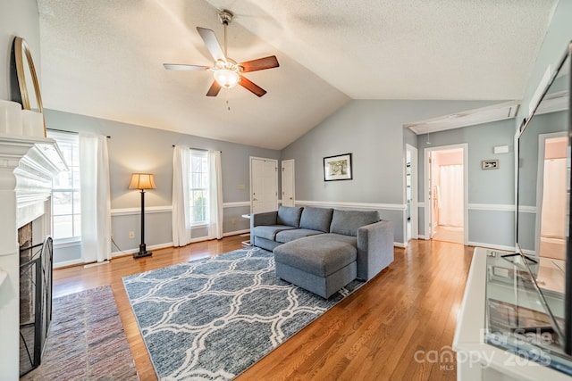 living area featuring lofted ceiling, a textured ceiling, ceiling fan, a fireplace with flush hearth, and wood finished floors