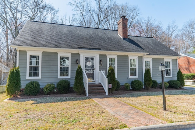 cape cod home with roof with shingles, a chimney, and a front yard