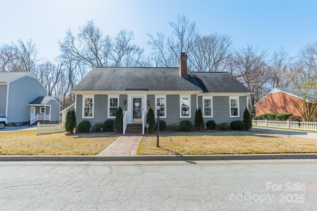 view of front of property with roof with shingles, a chimney, a front yard, and fence