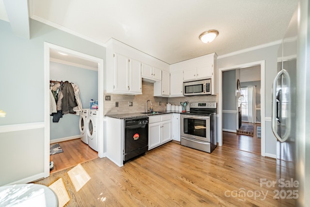 kitchen featuring washing machine and clothes dryer, light wood-style flooring, appliances with stainless steel finishes, white cabinets, and a sink