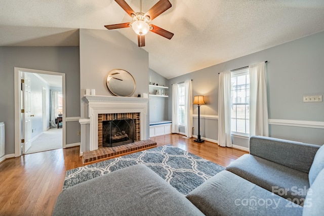 living room featuring vaulted ceiling, a fireplace, a textured ceiling, and wood finished floors