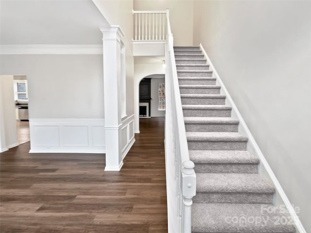 stairway featuring a wainscoted wall, crown molding, decorative columns, and wood finished floors