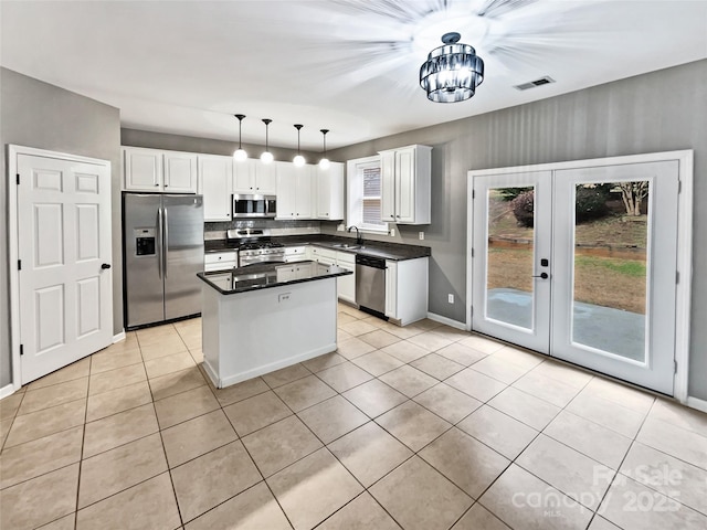 kitchen featuring a center island, pendant lighting, stainless steel appliances, dark countertops, and white cabinetry