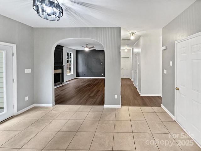 empty room with light tile patterned floors, ceiling fan, arched walkways, a fireplace, and baseboards