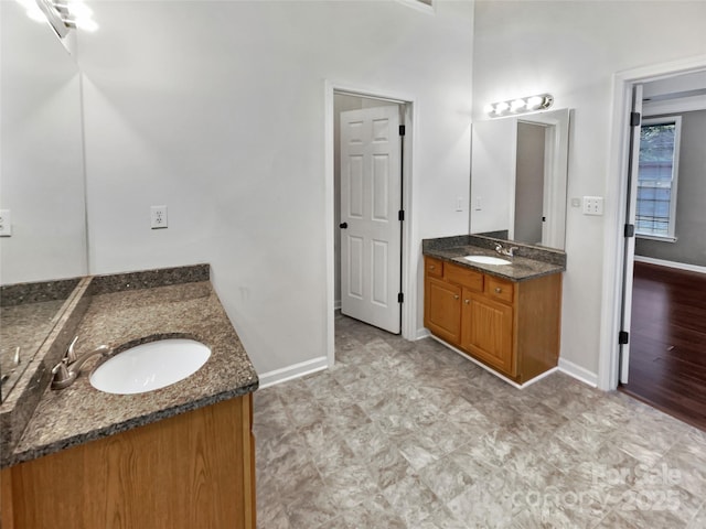 full bathroom with two vanities, a sink, and baseboards