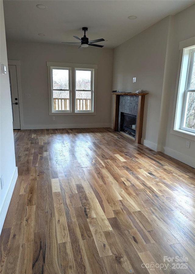 unfurnished living room featuring baseboards, wood finished floors, a ceiling fan, and a tile fireplace