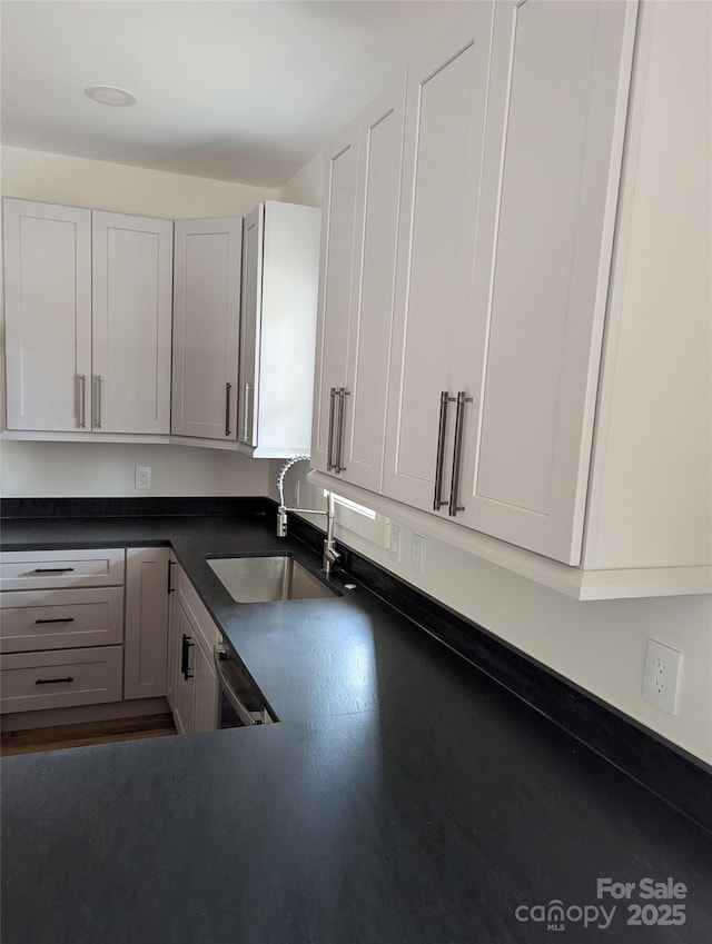 kitchen with dark countertops, white cabinets, dishwashing machine, and a sink