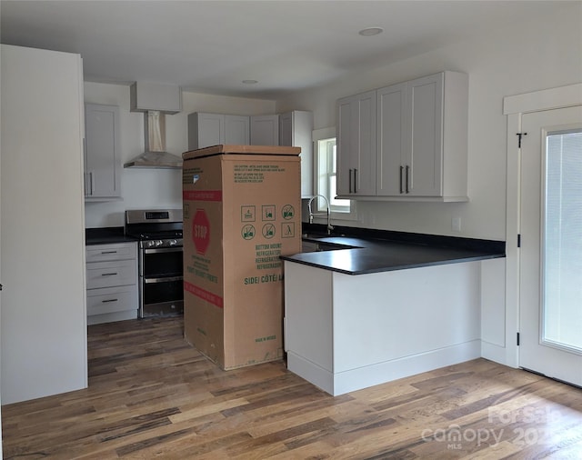 kitchen featuring dark countertops, wall chimney range hood, double oven range, a peninsula, and wood finished floors