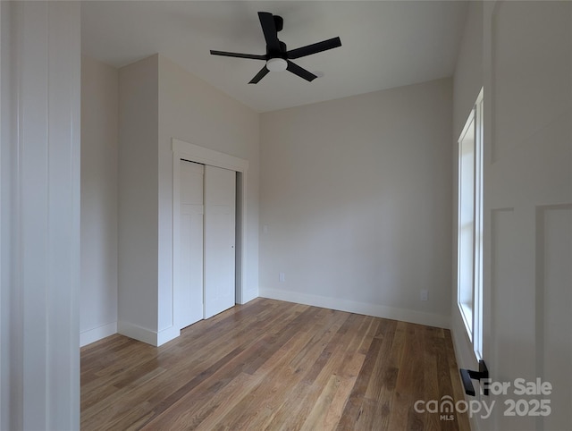 unfurnished bedroom with a ceiling fan, wood finished floors, baseboards, and a closet