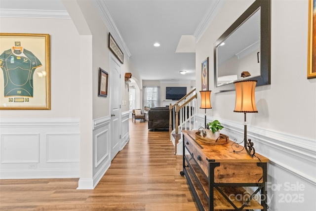 corridor with arched walkways, a decorative wall, ornamental molding, stairway, and light wood finished floors