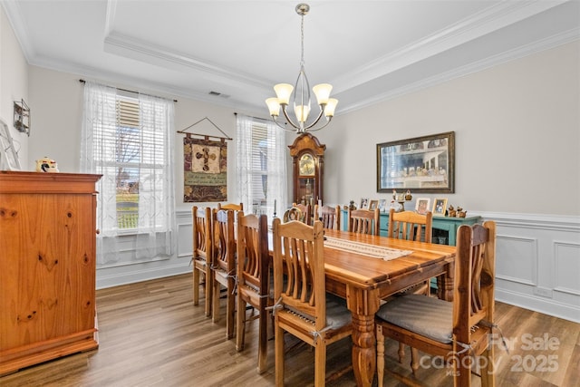 dining space featuring visible vents, wainscoting, light wood-style flooring, ornamental molding, and a tray ceiling