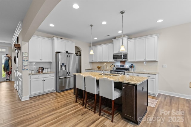 kitchen with light wood-style floors, appliances with stainless steel finishes, arched walkways, and a sink