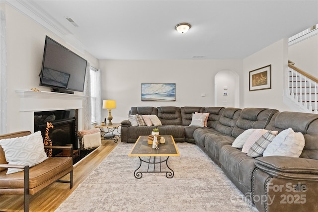 living area featuring arched walkways, visible vents, a glass covered fireplace, wood finished floors, and stairs