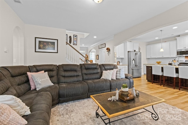 living area featuring arched walkways, recessed lighting, stairs, light wood finished floors, and crown molding