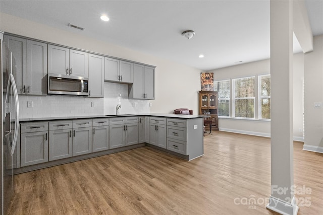 kitchen with a peninsula, appliances with stainless steel finishes, light wood-type flooring, and gray cabinetry