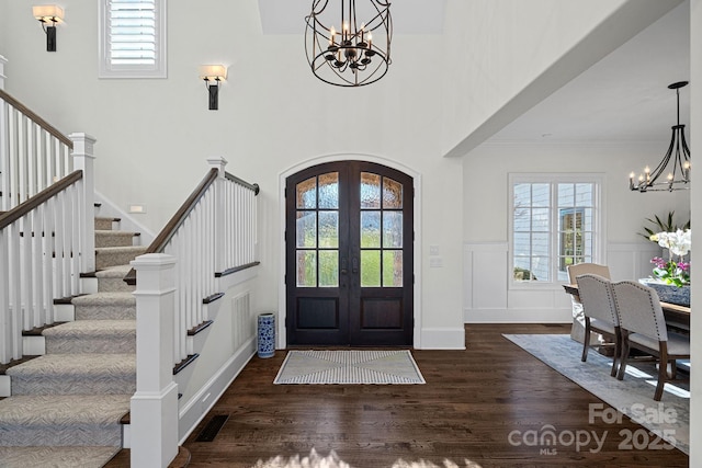 foyer entrance featuring arched walkways, stairway, dark wood-style flooring, french doors, and a notable chandelier