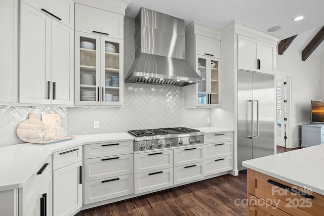 kitchen featuring stainless steel appliances, light countertops, glass insert cabinets, white cabinetry, and wall chimney range hood