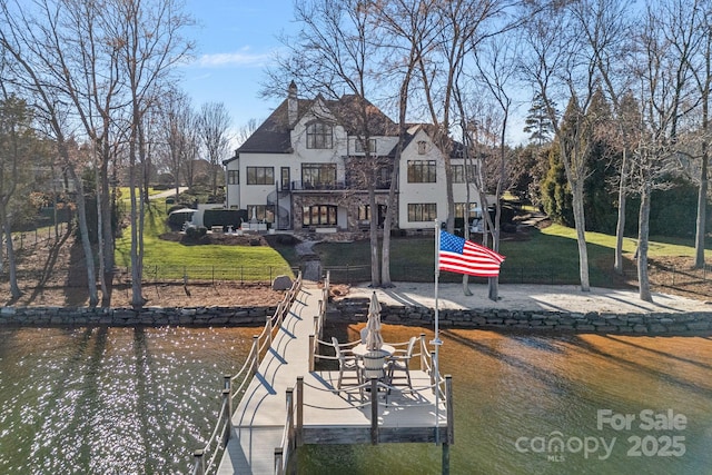 dock area with a water view, a lawn, and a balcony