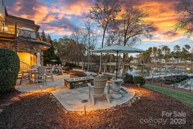 patio terrace at dusk with stairs, a dock, a water view, and a balcony