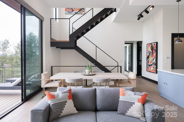 living room with a towering ceiling, baseboards, light wood-style floors, stairway, and rail lighting