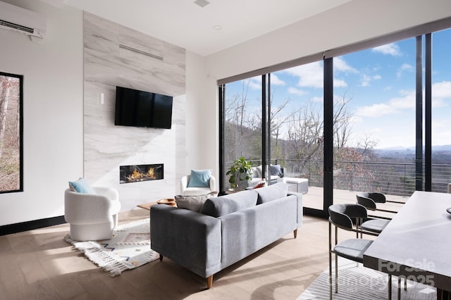 living room with an AC wall unit, light wood finished floors, a premium fireplace, and baseboards