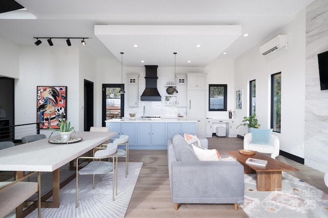 living area with a wall unit AC, recessed lighting, a towering ceiling, light wood-style floors, and rail lighting