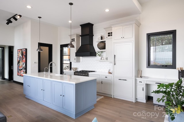 kitchen featuring premium range hood, a sink, white cabinets, light countertops, and glass insert cabinets