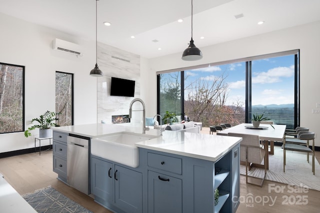 kitchen featuring a center island with sink, light countertops, stainless steel dishwasher, pendant lighting, and a sink