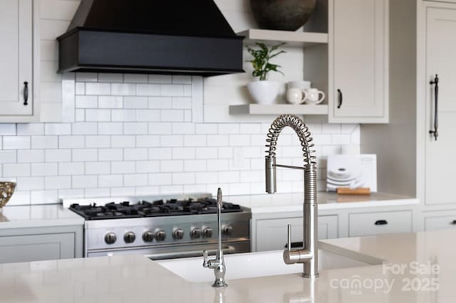 kitchen with custom exhaust hood, high end stainless steel range, light countertops, backsplash, and white cabinetry