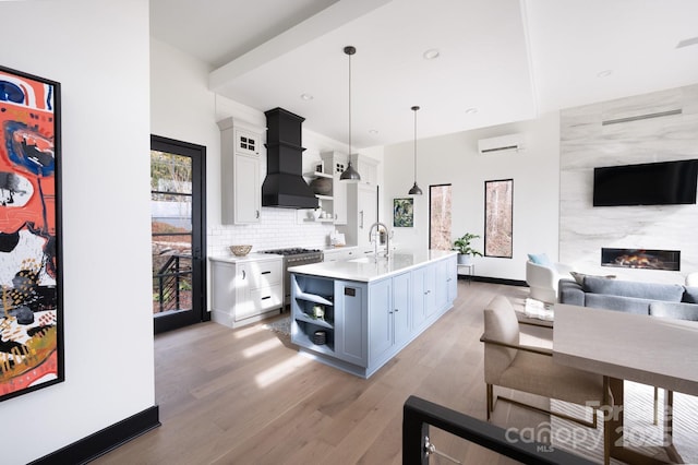 kitchen featuring open shelves, light countertops, hanging light fixtures, white cabinets, and an island with sink