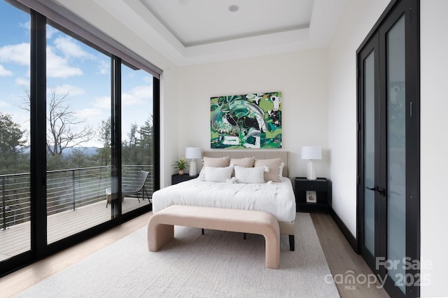 bedroom with access to outside, a raised ceiling, baseboards, and wood finished floors