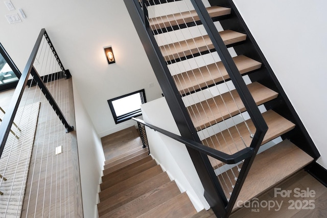 stairs featuring a towering ceiling, baseboards, and wood finished floors